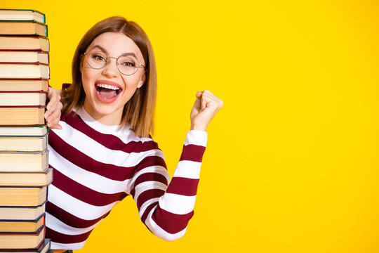Young woman in stylish striped pullover expressing happiness while standing by book on vibrant yellow backdrop