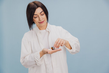 Middle aged woman Pouring Pills from a Bottle on Light Blue Background