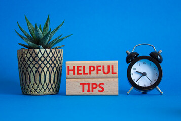Helpful tips symbol. Wooden blocks with words Helpful tips. Beautiful blue background with alarm...