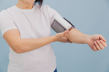 Woman measuring blood pressure with portable blood pressure monitor on a blue studio background