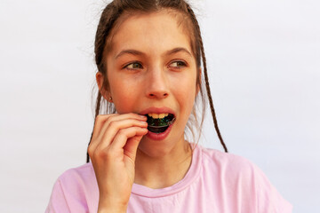 Young girl in pink t-shirt putting orthodontic plate on teeth with uneven teeth, malocclusion on white background. Concept orthodontic treatment