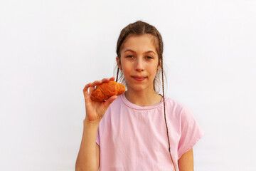 Playful cheerful red-haired girl with hair tied in ponytail holds two croissants in hands, looks at camera, isolated on white background.