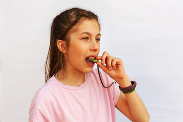Young girl in pink t-shirt putting orthodontic plate on teeth with uneven teeth, malocclusion on white background. Concept orthodontic treatment