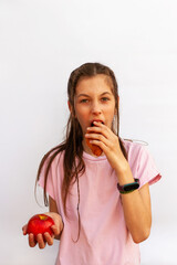 Girl in pink t-shirt holds delicious croissant in one hand and red apple in the other on white background. Healthy eating concept. Vertical photo