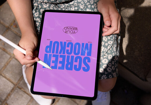 Individual holds a blank tablet outdoors, ready to create, with a stylus in hand. Screen mockup ready to use