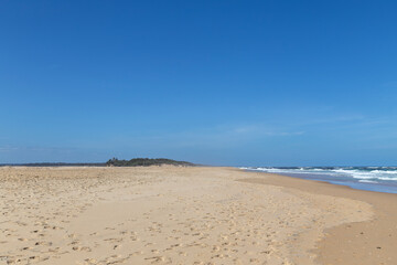Wide sandy beach at Lake Tyers, Victoria, Australia. Footprints in golden sand, gentle waves, clear blue sky and coastal dunes in a peaceful, natural setting. Ideal remote travel destination.