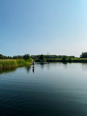 At this moment, a person is enjoying a leisurely ride on a paddle board while gliding across the calm waters of a beautiful lake, taking in the wonderful surroundings and sunshine