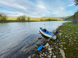 A brightcolored kayak rests peacefully on the sandy shore of a beautiful river, its vibrant hues contrasting nicely with the surrounding greenery and the shimmering water
