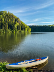 Obraz premium A bright yellow kayak is resting peacefully on the sandy shore of a tranquil lake, surrounded by trees and nature, inviting adventurous souls to take it out on the water