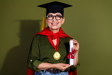 Smiling mature woman in graduation cap holding diploma celebrating achievement on green background...