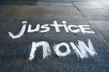 Justice Now: Urgent plea written in chalk on pavement demanding immediate action.