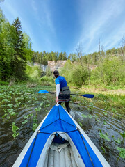A skilled man gracefully paddles a vibrant blue and white kayak along a tranquil river, savoring the breathtaking scenery and the exhilarating thrill of his exciting outdoor adventure