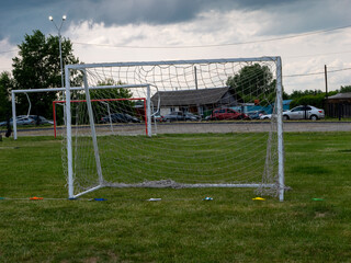 A soccer goal is in the middle of a field with a cloudy sky above