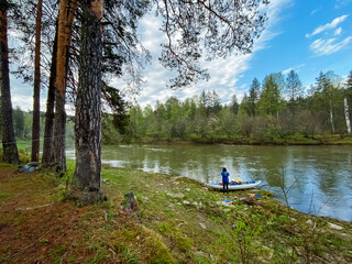 A person is sitting in a kayak on the sandy shore of a beautiful river, surrounded by lush trees and the stunning natural landscapes that define the wilderness and forested areas