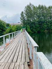 A charming wooden bridge gracefully spans over a tranquil body of water, surrounded by lush trees that provide shade and beauty to the scene, creating a picturesque landscape