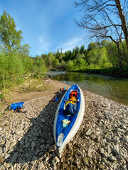 A vibrant blue and white kayak is currently resting on the rocky shore near a flowing river, creating a picturesque scene that captures the essence of outdoor adventure and recreation