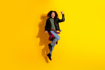 Energetic young man jumping with joyful expression on a vibrant yellow backdrop showcasing fashion...