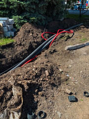 A chaotic mess of electrical wires is haphazardly scattered in the dirt, looking extremely disorganized and untidy, likely due to recent construction or repair work taking place nearby