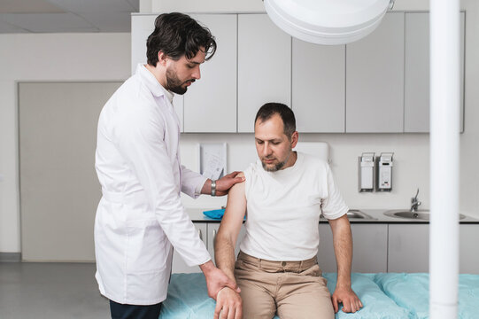 Doctor examining male patient with shoulder pain during physical assessment in clinic, concept of musculoskeletal disorder, orthopedic diagnosis, injury treatment, physical therapy and rehabilitation 