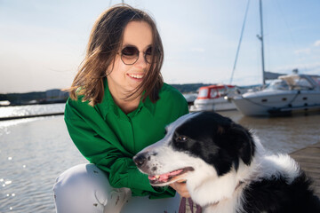  A girl with a bob haircut in a green shirt and white trousers walks her dog on a pier in Norway. Sunglasses and a yacht in the background complete this calm, free-spirited moment.