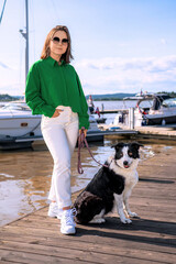 woman and her dog. A sunny day in Norway: a stylish girl in sunglasses walks her dog along the pier. A yacht and the sea behind — a shot about harmony with self and nature.