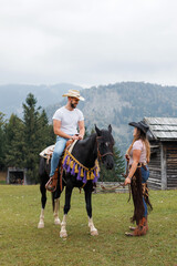 Obraz premium Cowgirl instructor, holding the reins, watching and helping a young rider mount his horse at the ranch riding school