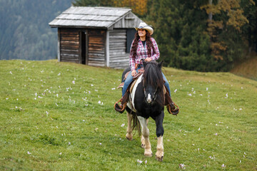 Authentic western scene of a confident cowgirl on horseback, riding through scenic mountain terrain under a light mist