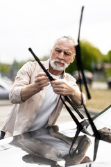 Handsome senior man replacing windshield wipers on car
