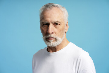 Serious senior man with white beard and hair posing on blue background