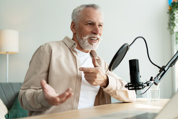Senior radio host broadcasting in home studio, gesturing, using microphone