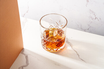 Whiskey with ice cube in the glass at white table.