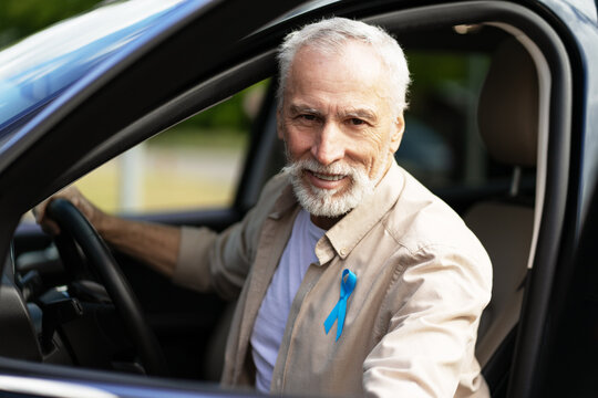 Senior man driving car wearing blue awareness ribbon: prostate cancer awareness month