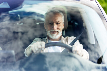 Senior man driving modern car and smiling looking at camera