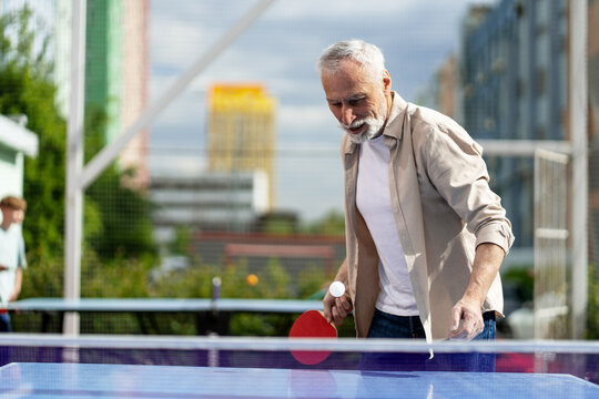 Happy senior man playing ping pong outdoors in urban city