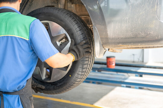 Action from back of a technician man is installing a car wheel after new tire replacement. Working person scene, selective focus.