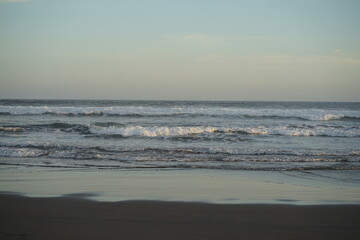 Obraz premium Serene Coastal Scene Ocean Waves Gently Rolling onto Sandy Shore at Sunset