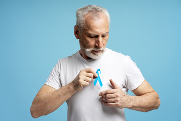 Senior man showing blue ribbon for prostate cancer awareness month