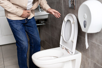Senior man experiencing abdominal discomfort in bathroom near toilet