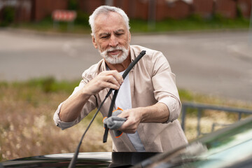 Senior man cleaning windshield wipers with microfiber cloth