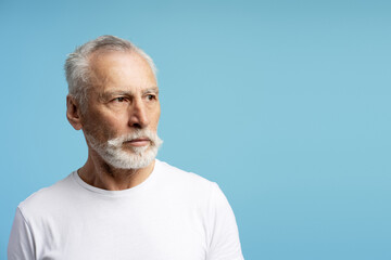 Senior man looking away on blue background conveys thoughtfulness