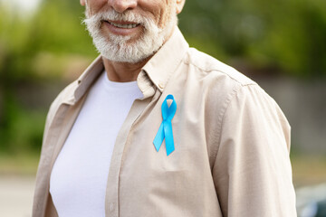 Senior man wearing blue ribbon for prostate cancer awareness month, colon cancer closeup