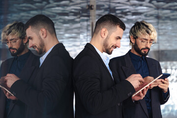Two young businessmen wearing suits focused on digital tablets while collaborating in a modern, stylish office space with reflective glass walls and a professional, tech-driven atmosphere. 
