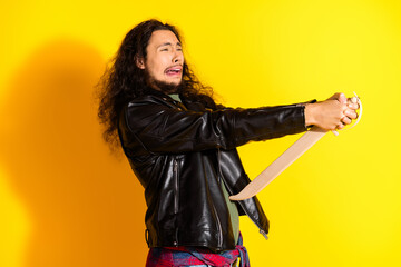 Young man in black leather jacket posing with expressive gesture against vibrant yellow background,...