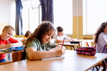 Portrait of a grirls sitting in school bench and writing in classroom.