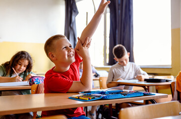 Boy raising hand to answer teacher's question during class in classroom.