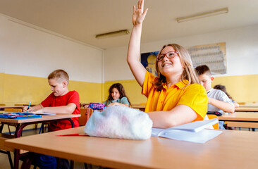 Girl raising hand to answer teacher's question during class in classroom.