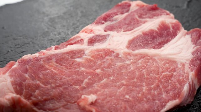Another single piece of pork rests on a dark slab. The rotation reveals the fine distribution of fat.