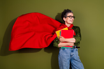Confident senior woman with short grey hair posing with notebooks and a red cape on khaki...