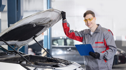 Portrait happy male auto mechanic in uniform inspecting car engine in workshop, industry worker