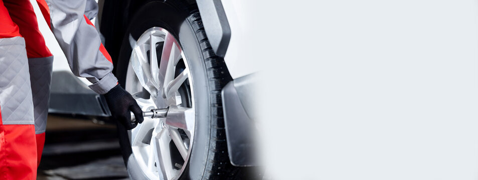 Auto mechanic changing car winter tire in service garage, banner with copy space